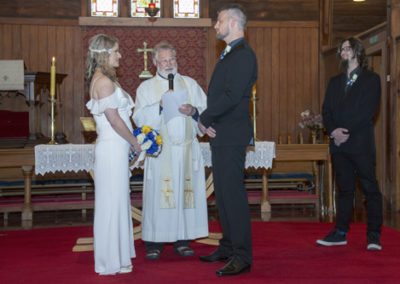 bride & groom looking at each other seriously as celebrant is speaking in historic wooden church with candles