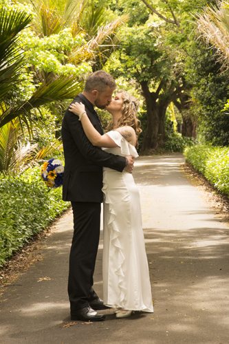 bride & groom embracing & kissing in leafy nikau palm lined lane