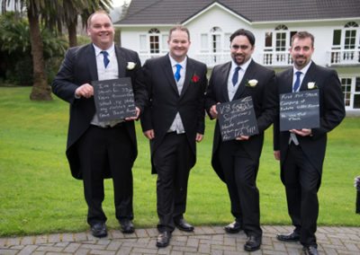 smiling groomsmen with blackboards outdoors at Wallaceville House