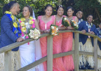 Colourful Tokelauan wedding, happy bridal party leaning on rustic wooden bridge