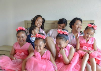 Colourful Tokelauan bridesmaids and flower girls laughing and smiling on a double bed