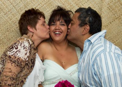 Closeup of parents kissing laughing bride on her cheeks