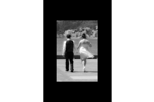 Black & white of windswept bride and groom walking away on Wellington waterfront