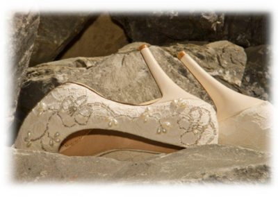 closeup of bride's beaded stiletto shoes lying on rocks on waterfront