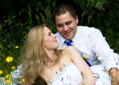 bride & groom lying in grass and dandelion flowers gazing lovingly at each other