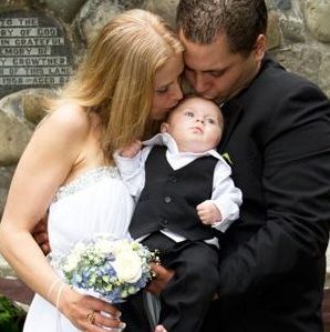 outdoors wedding with bride and groom both kissing their baby