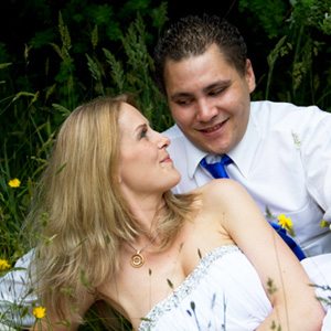 bride & groom laying in grass and dandelion flowers smiling lovingly at each other