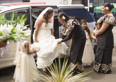 bridesmaids holding gown to help bride out of car on arrival at church