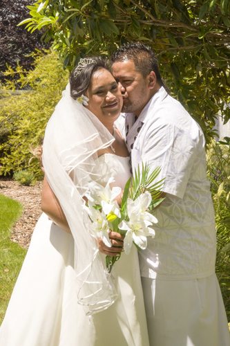 Beautiful Samoan couple, groom kisses bride on cheek in garden setting