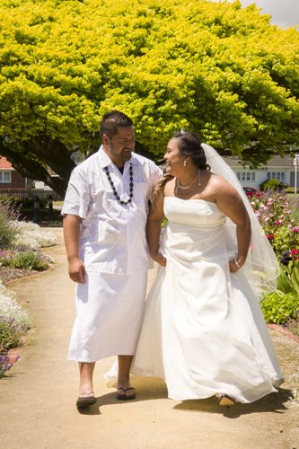 Samoan bride & groom laughingly gaze at each other as they walk in sunny garden path
