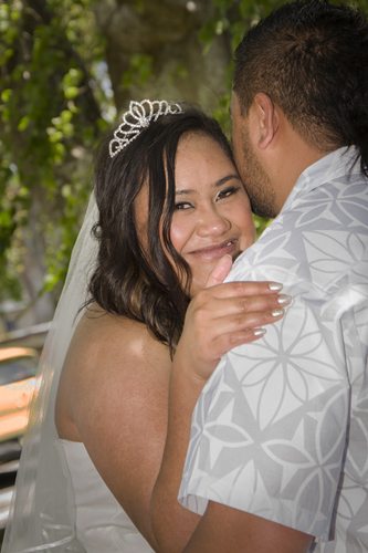 Beautiful Samoan couple, closeup of bride smiling over groom's shoulder as they embrace in garden setting