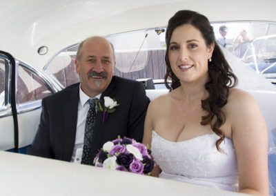 Smiling bride & dad in back of classic car on way to Pencarrow Lodge wedding