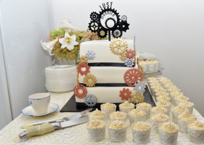 cogs & gears themed wedding cake surrounds by cupcakes