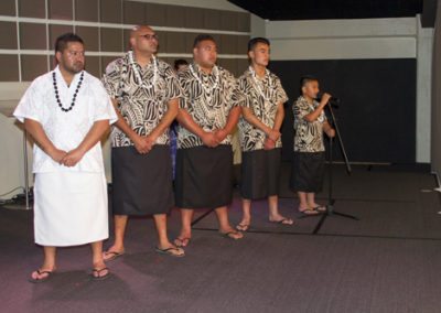 Samoan wedding, groom & groomsmen standing onstage, as son sings for bride as she walks down the aisle