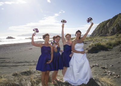 Pencarrow Lodge wedding bride & bridesmaids raise their bouquets and cheer on beach