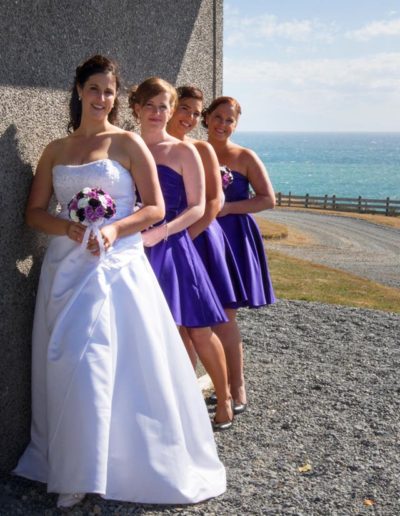 Pencarrow Lodge wedding bride & bridesmaids lined up against side of lodge, with choppy sea in background