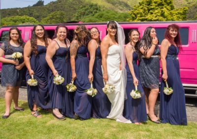 Maori bride & bridesmaids joking around beside pink limo