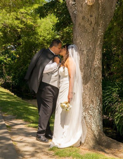 Maori bride & groom kiss by tree along gravel path