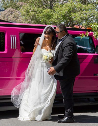 Maori bride & groom embrace beside pink limo