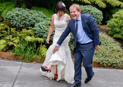 laughing groom lifting wedding gown to show bride's special red and black stiletto shoes