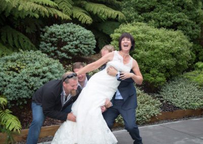 laughing bride being picked up by groom and her brothers in bush setting