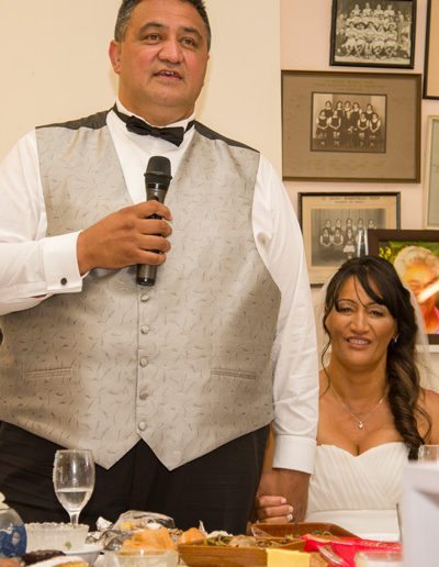 Maori bride & groom hold hands during wedding reception speeches at marae