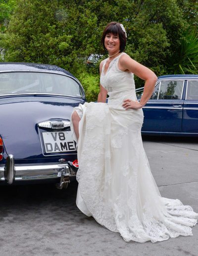 sassy bride with foot up on bumper of Daimler car,showing some leg and red & black shoe