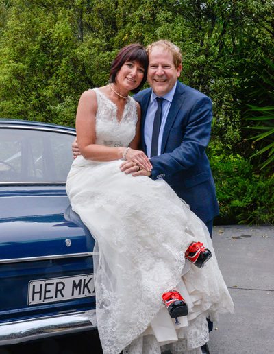 bride & groom embracing, with bride sitting on her mk II car, & showing red & black shoes