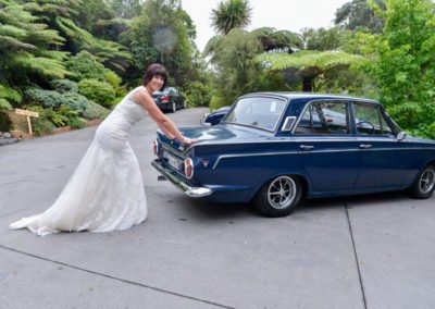 smiling bride pushing old blue mk II car in bush setting