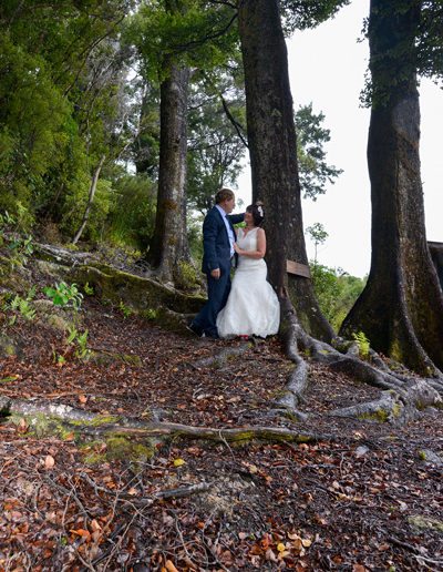 bride & groom in native bush setting embracing while leaning against tree