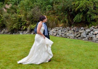 bride & groom walking arm in arm on lawn with rock wall behind, with bride holding dress up