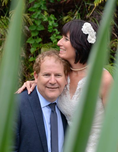 closeup of bride and groom embracing framed by flax in foreground