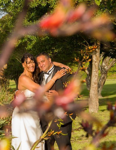 Maori bride & groom embrace in scenic park framed by harakeke flowers