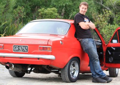 smiling young man leaning against side of red Ford Escort