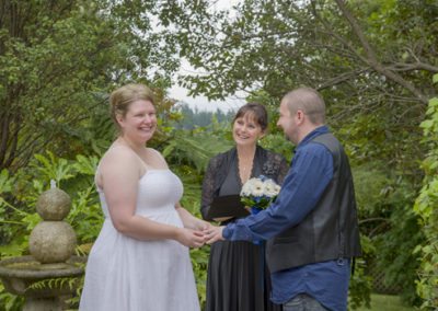 laughing bride & groom exchanging rings in garden with celebrant looking on