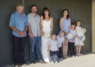 bride & groom & family group leaning against wooden wall at beach