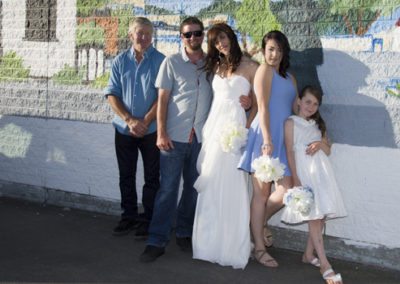 bride & groom & family group leaning against mural on beach wall