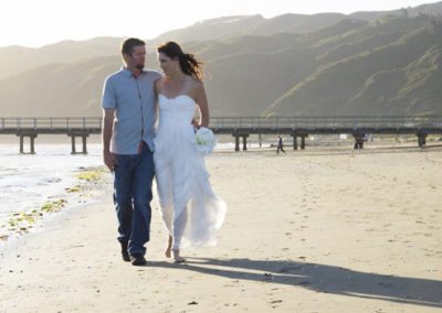 bride & groom walking arm in arm along beach with long sunset shadows