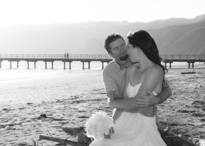 bride & groom embracing on sunny Petone beach with wharf in background