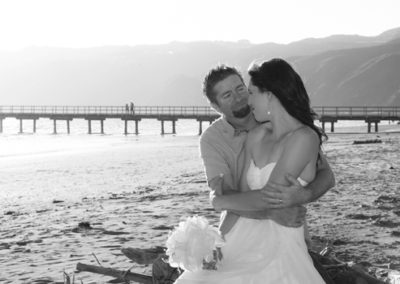 bride & groom embracing on sunny Petone beach with wharf in background