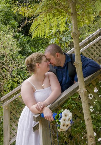 loving bride & groom in pretty nature setting, standing on steps, heads together