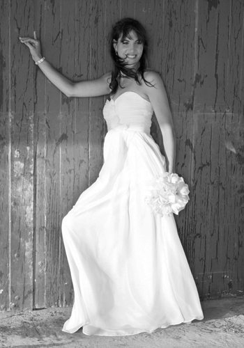B&W bride against wooden wall with wind blowing her hair and dress
