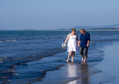 bride & groom holding hands while splashing barefoot at the edge of the sea