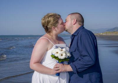closeup of bride & groom kissing on sunny beach