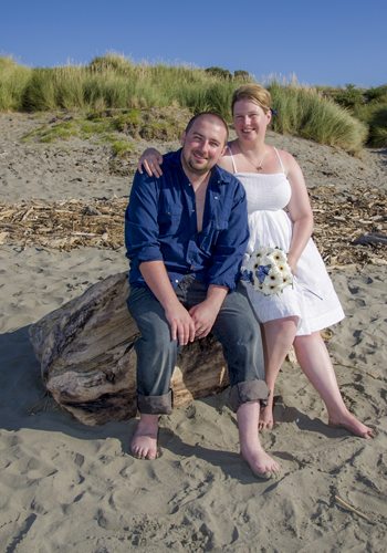 loving bride & groom sitting on driftwood at beach