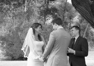 black & white bride & groom holding hands and laughing with celebrant as they make wedding vows