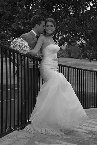 Black & white sexy bride leaning against fence & groom embracing her