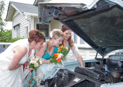 bride & colourful bridesmaids looking under bonnet of classic car