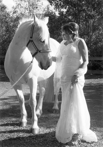 B&W romantic bride with white horse with its head turned to bride