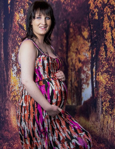 pregnant lady in colourful dress standing in front of autumn trees